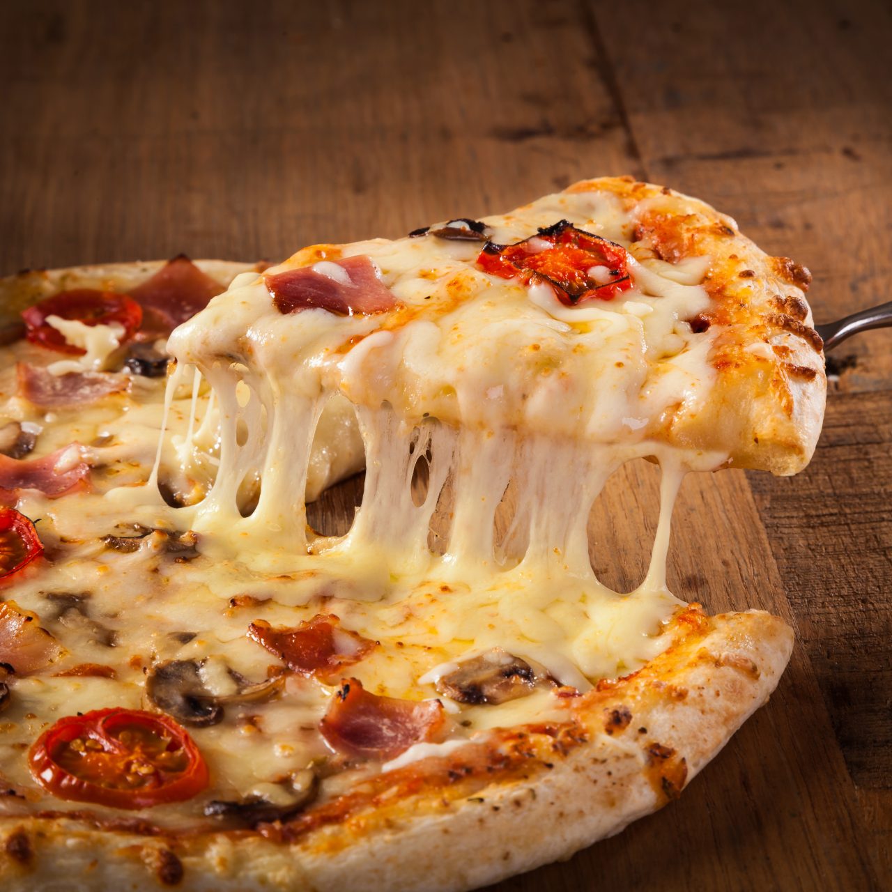 Hot,Pizza,Slice,With,Melting,Cheese,On,A,Rustic,Wooden